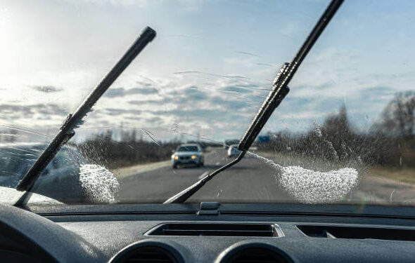 Car wipers clean windshields when driving in sunny weather, inside view.